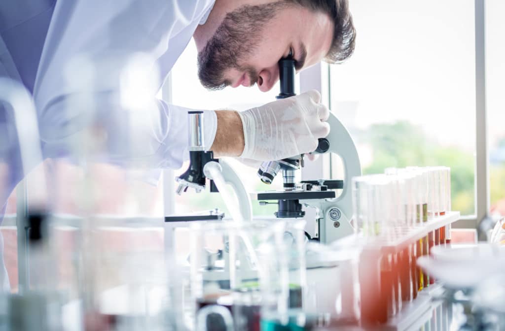 Scientists man working and look in to microscope in lab