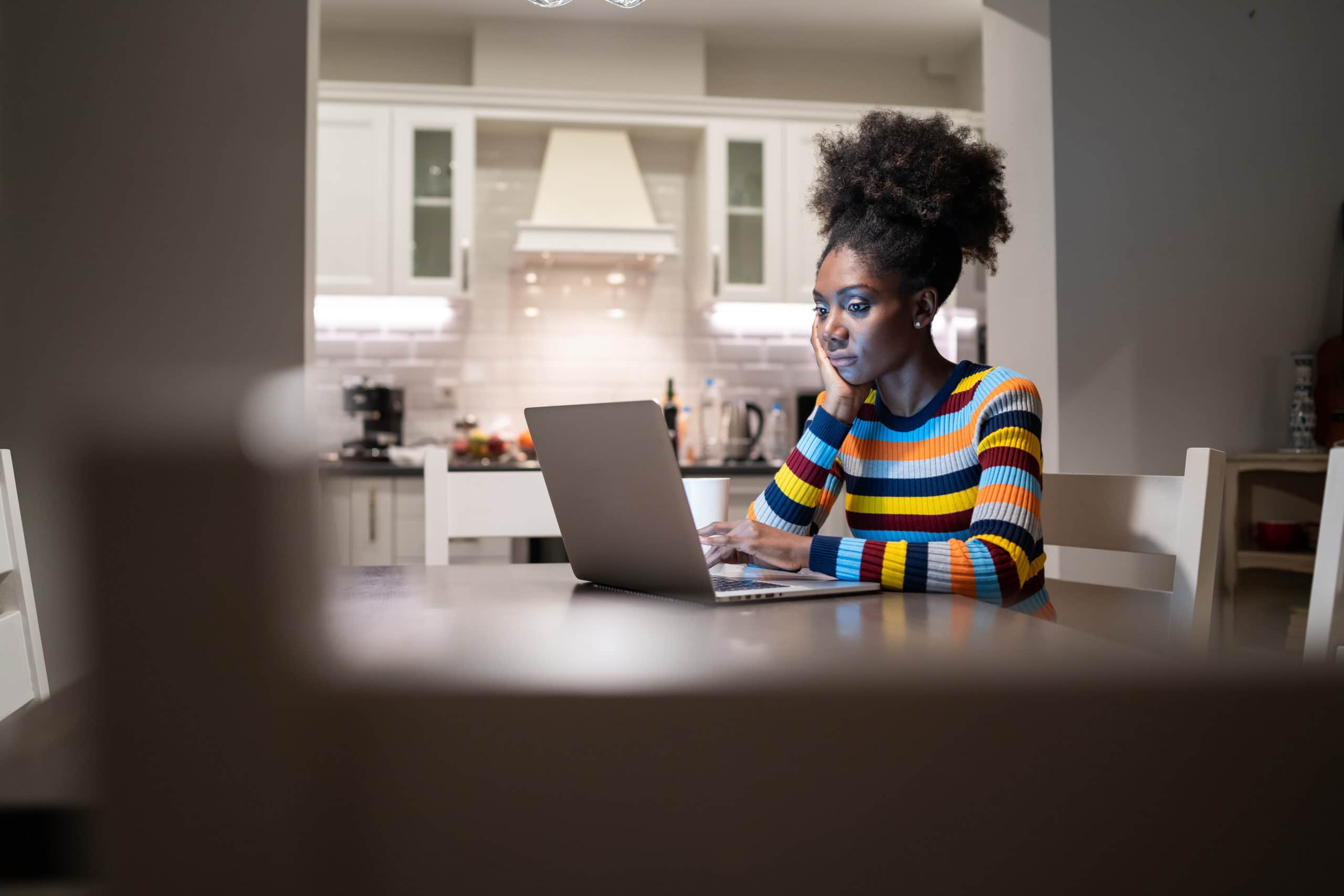 Woman using laptop at home at night while sitting at her kitchen table