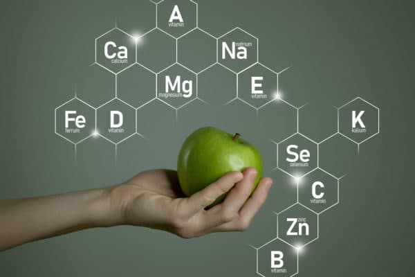 Person holding an apple with periodic table elements in the background