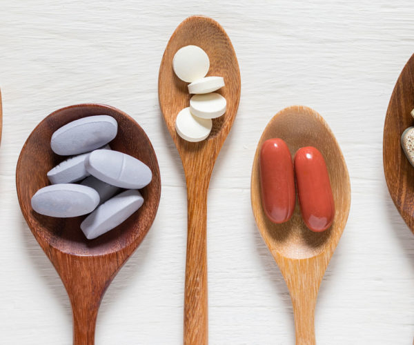 Wooden spoons holding different amounts of vitamins and supplements on a table