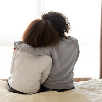 Rear back view mother embracing daughter that suffers from Mania