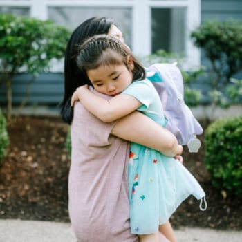A Korean woman holds her daughter tightly in an embrace, the girl showing anxious behavioral issues.