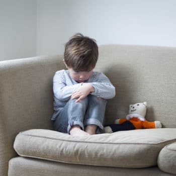 Little boy suffering from Autism sitting on the couch upset.
