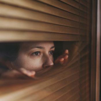 woman peeking through blinds afraid of the outside