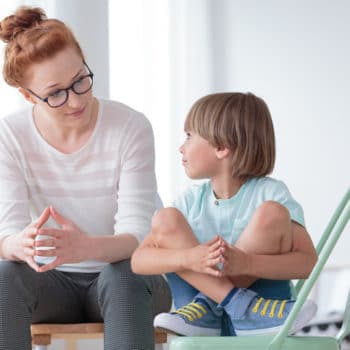 Young female psychologist having serious conversation with little boy suffering from PANDAS