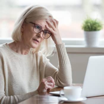 Mature woman holding her hand to her head. She appears confused from memory issues.