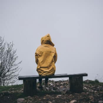 Rear view of depressed woman sitting alone on bench in yellow raincoat