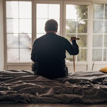 A lonely man is sitting on the bed. Representing someone with memory and dementia issues.